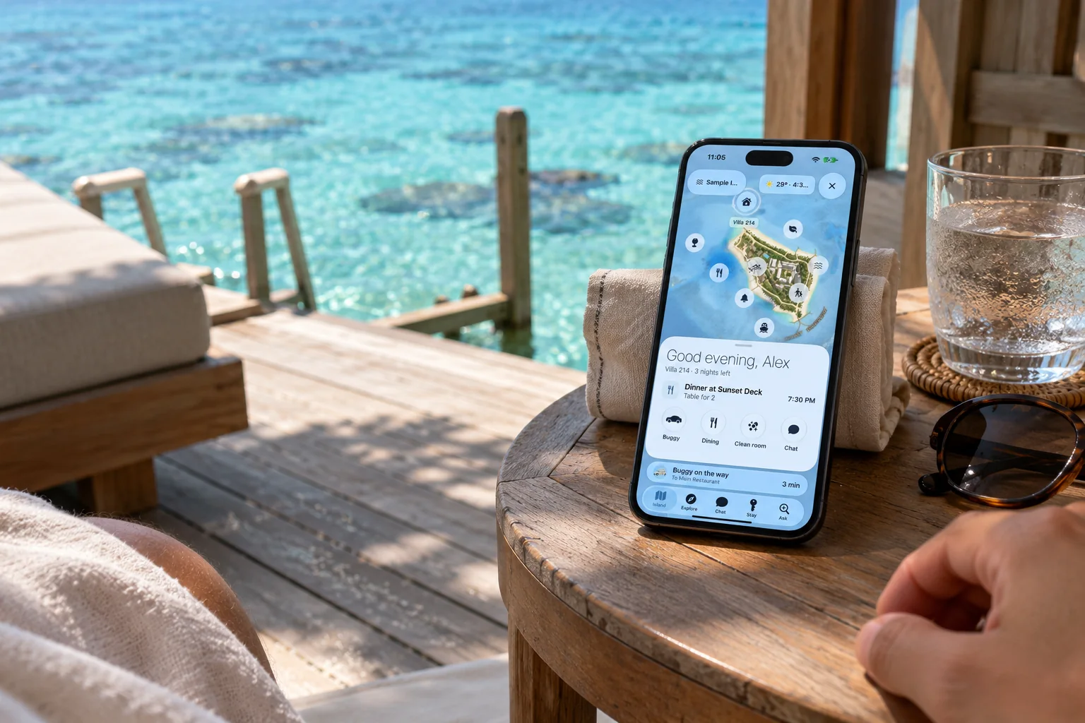A guest phone on a villa deck at golden hour showing the Coralis guest app.